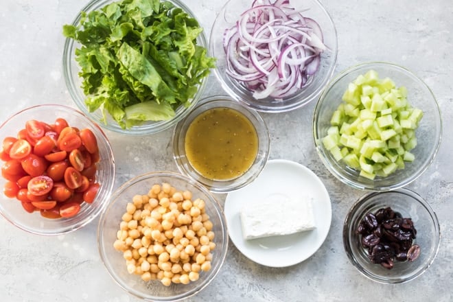 Mediterranean chopped salad ingredients in various clear bowls.