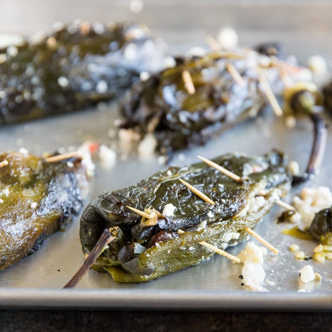 Roasted poblano chiles stuffed with a two-cheese filling and secured with toothpicks on a sheet pan.