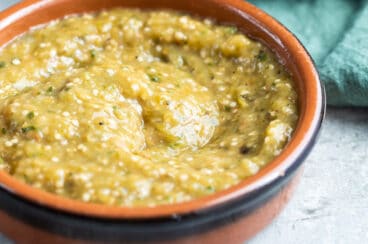 Chipotle tomatillo green chili salsa in a red bowl and a bowl of chips.