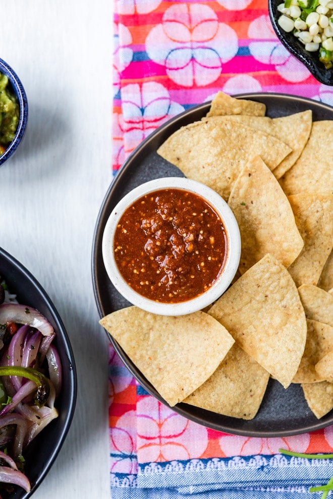 Copycat chipotle hot salsa in a white dish on a black plate with tortilla chips.