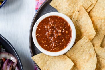 Copycat chipotle hot salsa in a white dish on a black plate with tortilla chips.