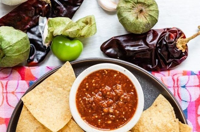 Copycat chipotle hot salsa in a white dish on a black plate with tortilla chips.