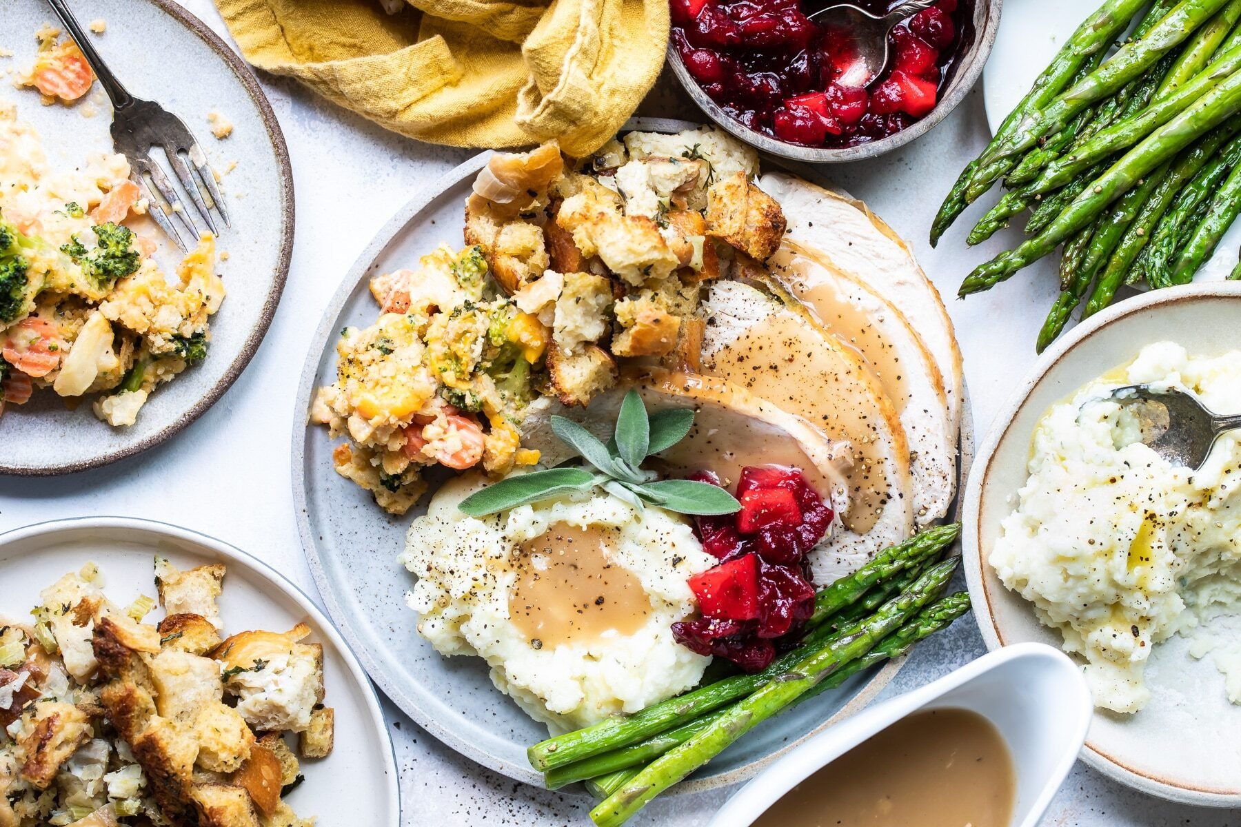 A plate of roasted trukey, stuffing, vegetables, mashed potatoes and gravy, and cranberries.