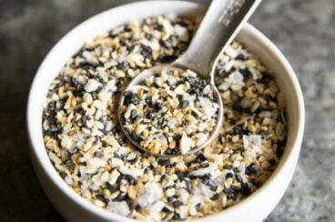 Everything bagel seasoning in a white bowl with a teaspoon.