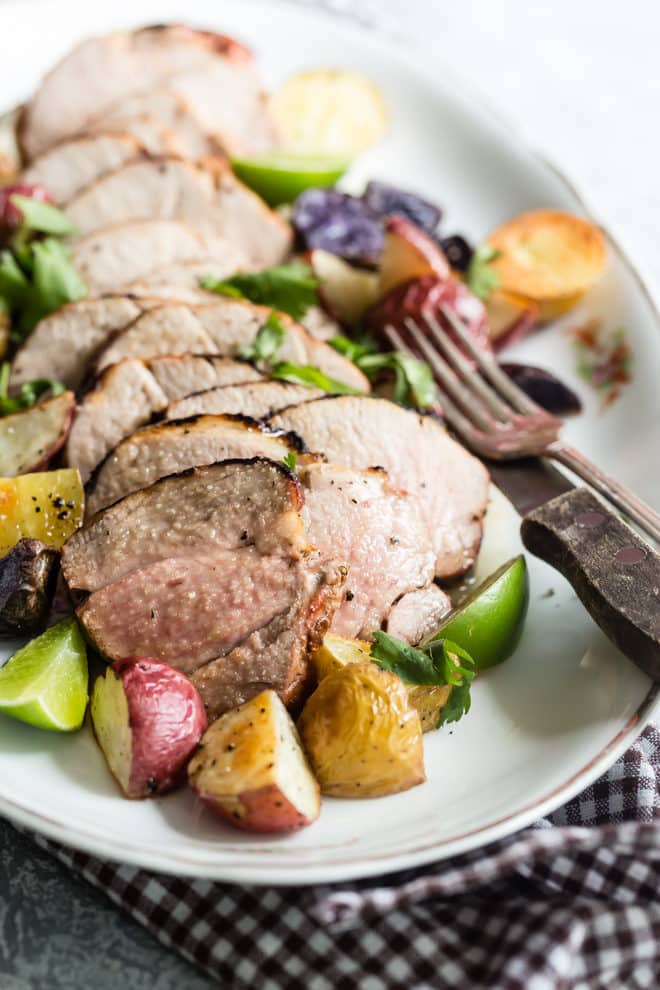 Grilled pork tenderloin and vegetables on a white platter.