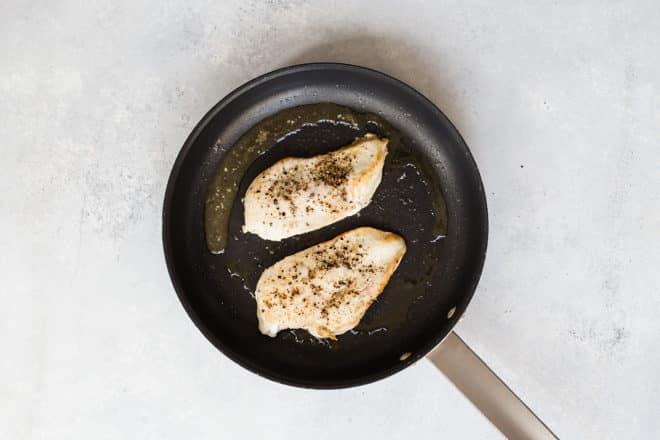 Chicken breast cooking in a skillet.