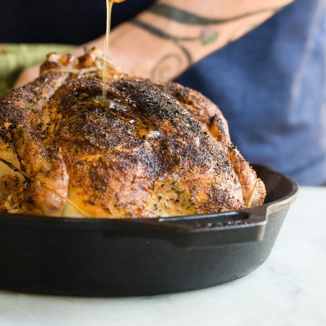 Sauce being drizzled onto rotisserie chicken in a cast iron skillet.