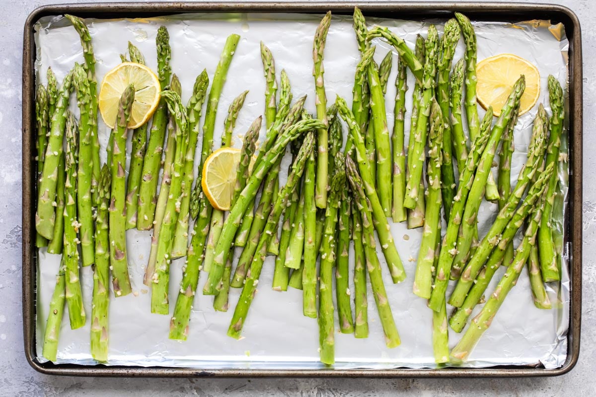 Raw asparagus on a rimmed baking sheet with lemon slices.