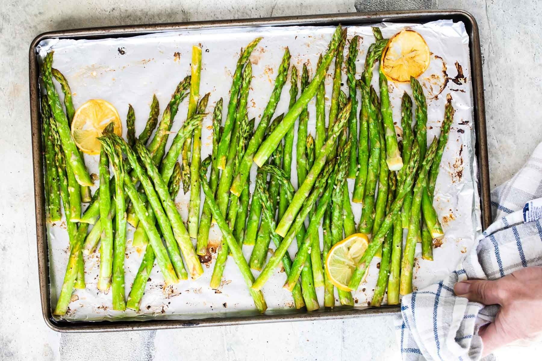 Roasted asparagus on a rimmed baking sheet with lemon slices.