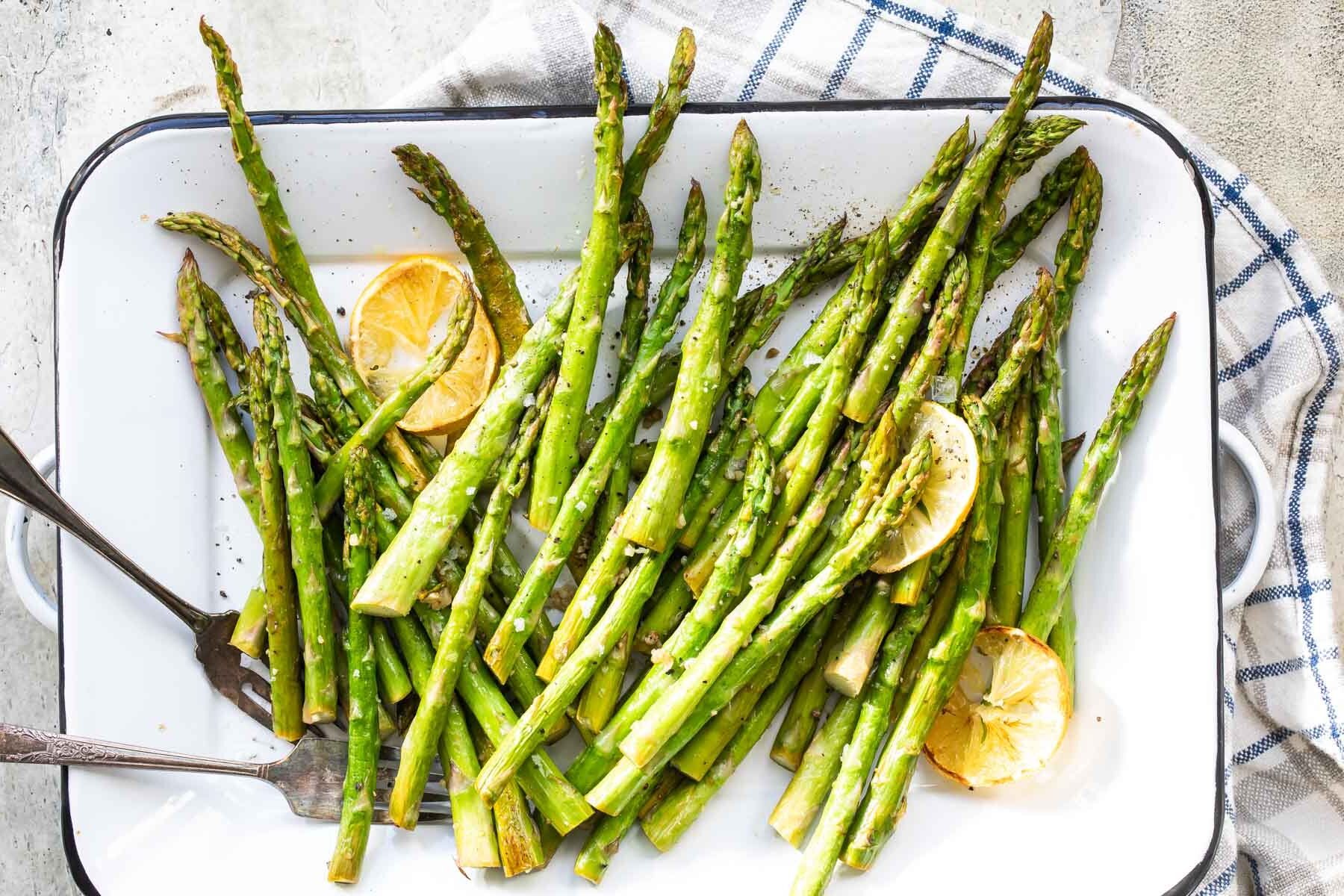 Roasted asparagus on a rimmed baking sheet with lemon slices.