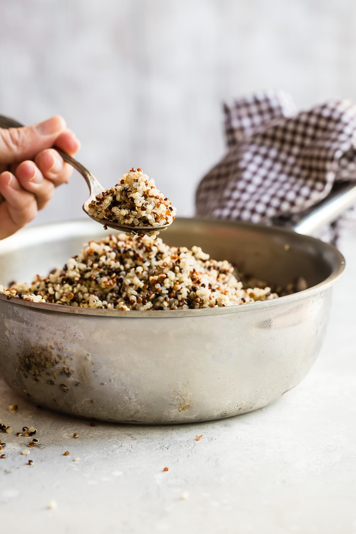 Cooked quinoa in a sliver bowl with someone spooning some out.