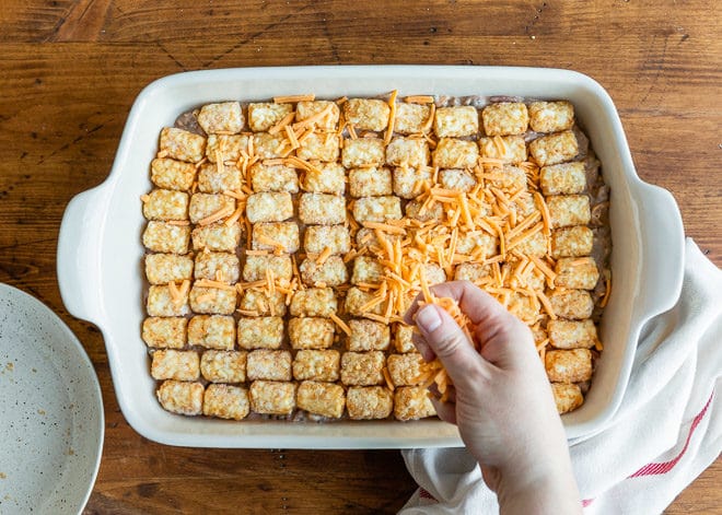 Cowboy Casserole being sprinkled with shredded cheese.