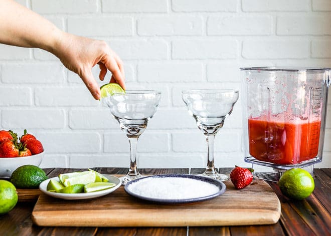 A person setting a lime on a margarita glass.