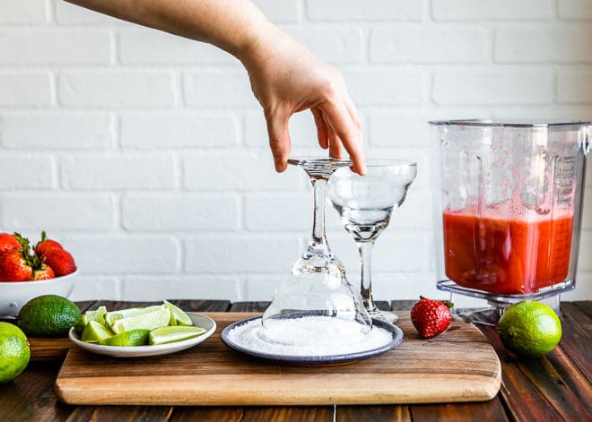A margarita glass being dipped on a plate of salt.