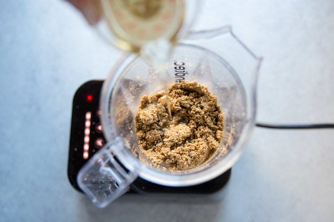 Someone drizzling oil into a blender of ground sesame seeds.