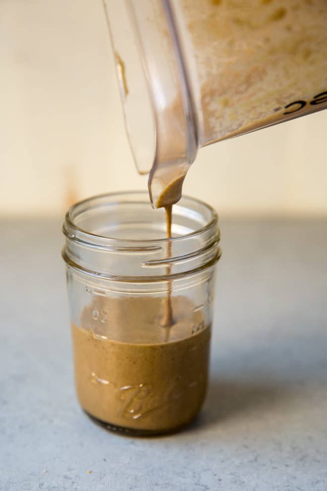 Tahini being poured out of a blender pitcher into a mason jar.