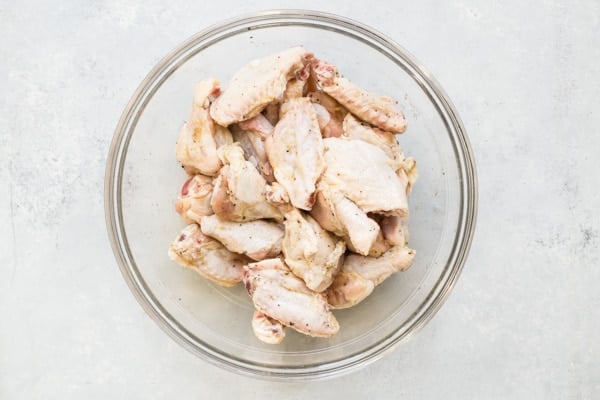 Raw chicken wings in a clear bowl.