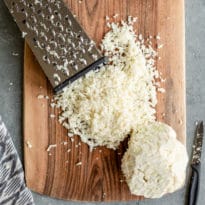 Shredded cauliflower on a wood cutting board.