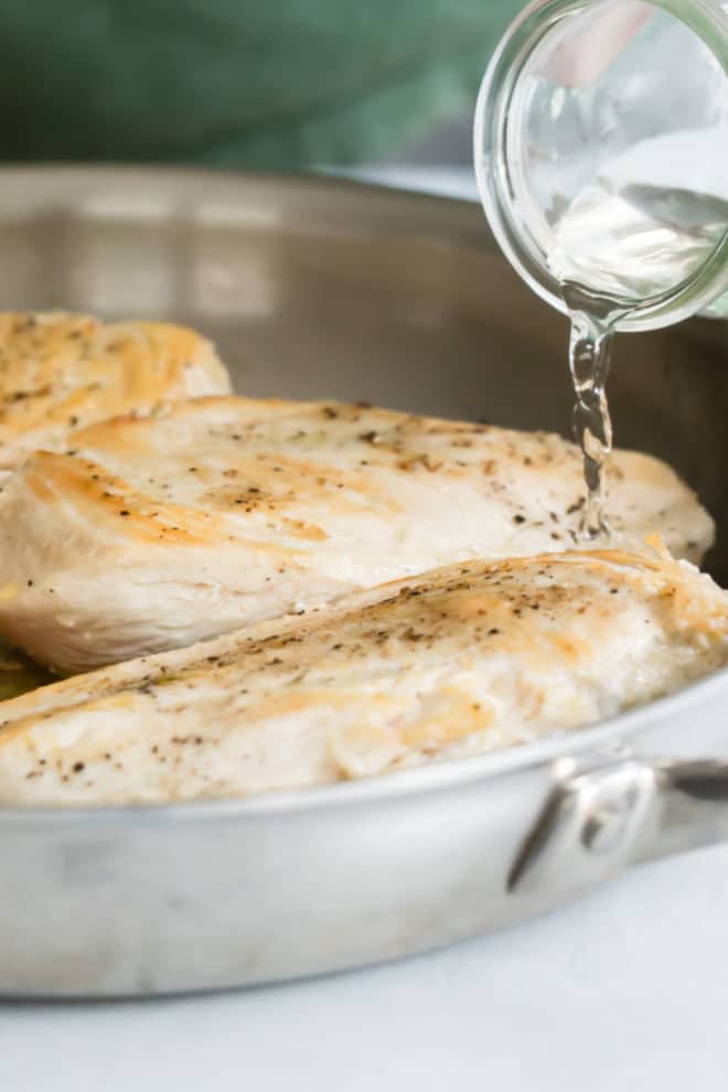 Water being poured into a silver skillet with cooked chicken.