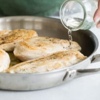 Water being poured into a silver skillet with cooked chicken.