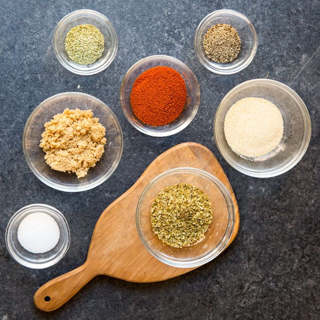 Grilled chicken rub ingredients in various bowls on a gray counter top.