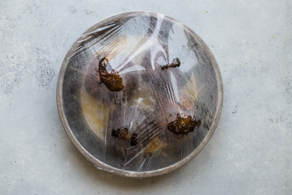 An overhead shot of beets in a round baking pan covered in saran wrap.