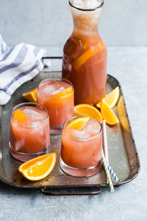 Three mocktails in clear glasses with a glass juice bottle on a metal tray.