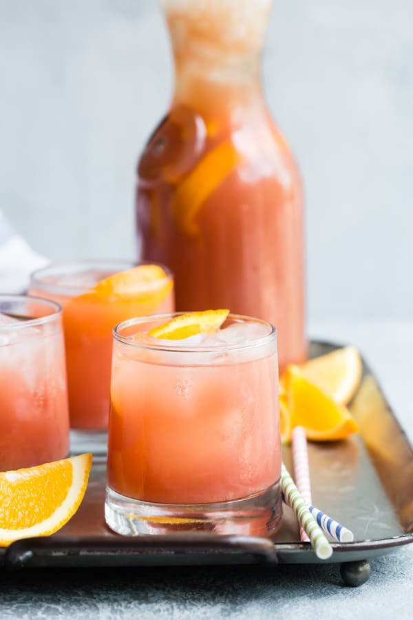 Three mocktails in clear glasses with a glass juice bottle on a metal tray.