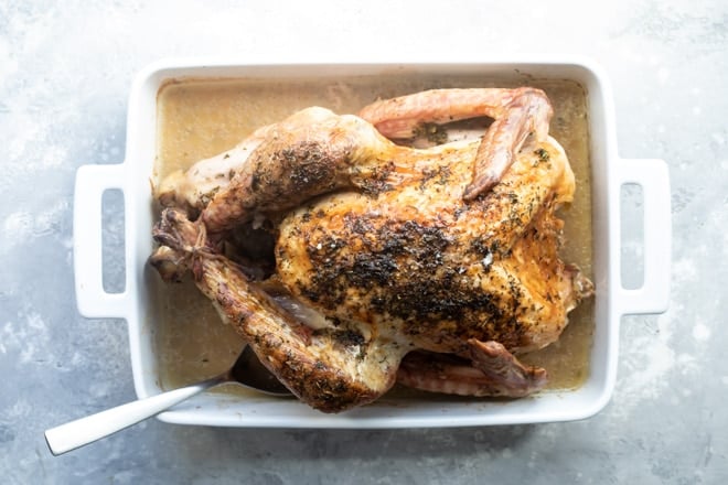Baked turkey with juices in a white baking dish with a silver spoon.