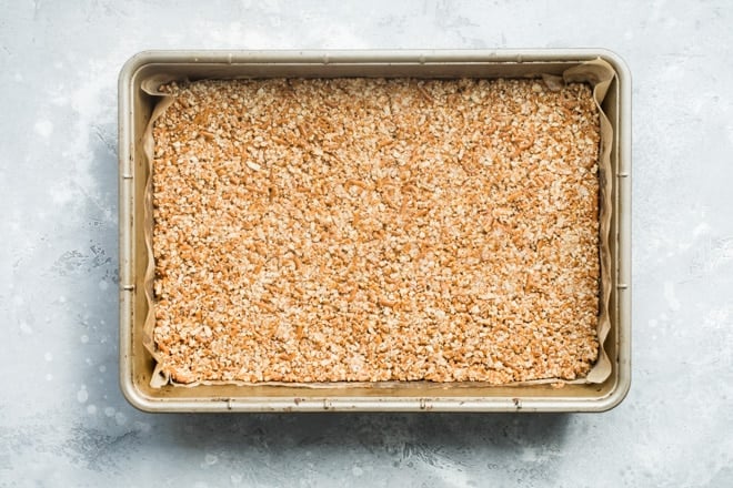 Smashed pretzel crust in the bottom of a tan baking pan.