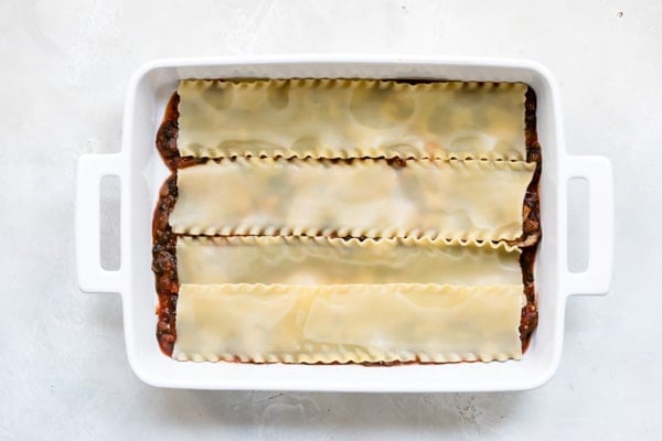 Vegetable lasagna ingredients being layered in a white baking dish.