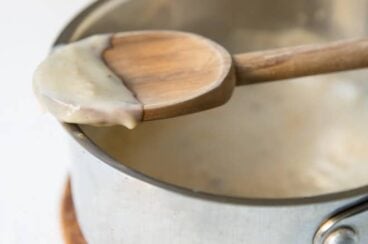 Condensed cream of chicken soup on a wooden spoon resting on a silver pot.
