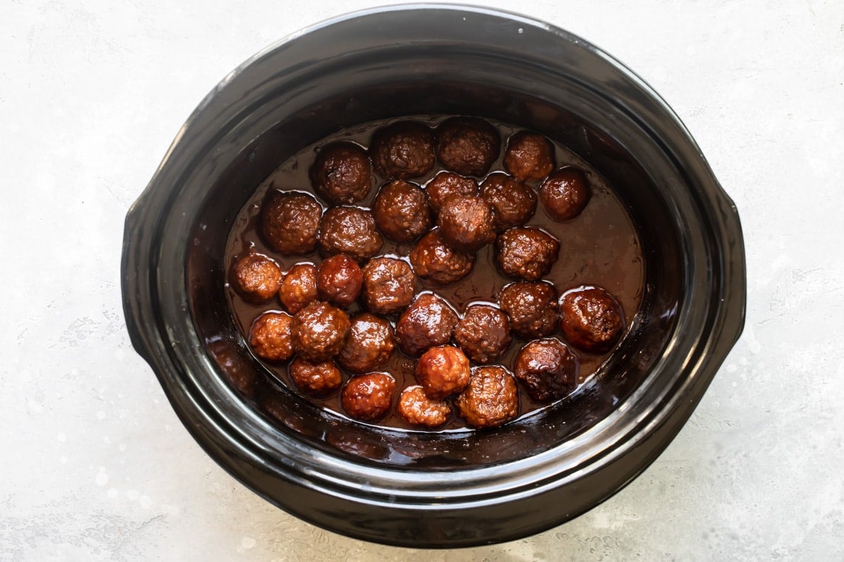 Crockpot meatballs with grape jelly sauce in a black slow cooker.