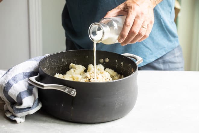 Milk being poured onto mashed potatoes in a black pot.