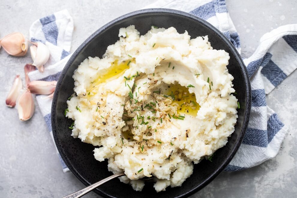 Garlic mashed potatoes in a black bowl with a serving spoon on a blue and white striped towel.