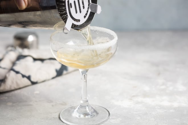 Sidecar cocktail being poured into a clear stemmed glass from a silver shaker.