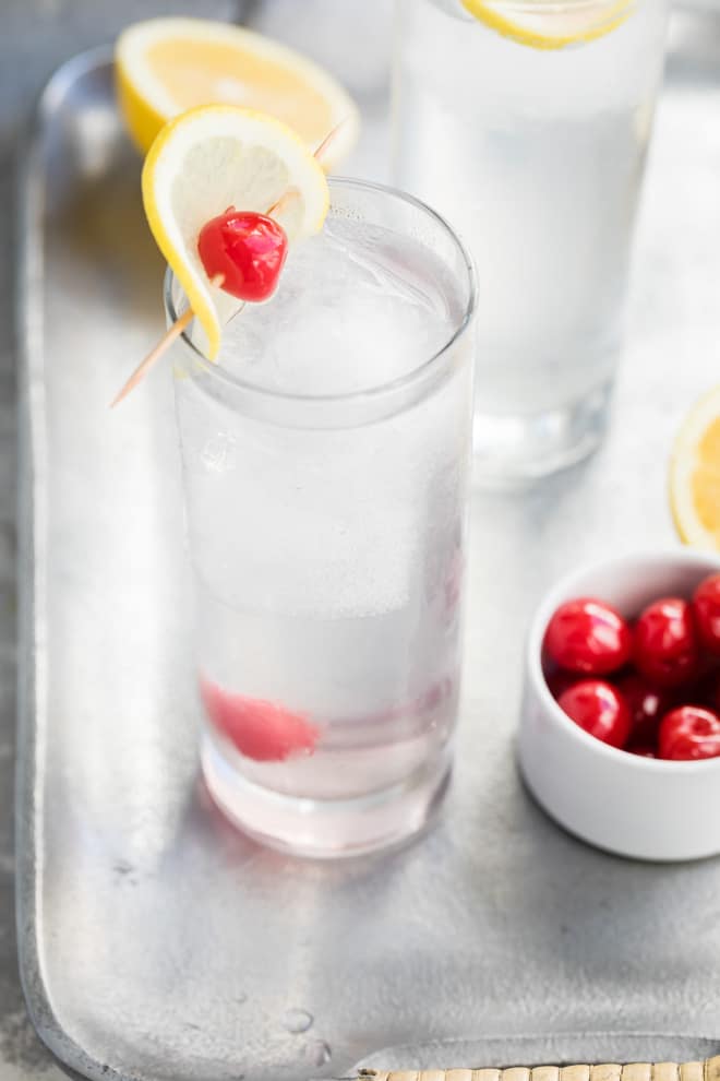 Tom collins in a clear glass with a lemon and cherry.