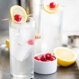 Tom collins in two clear glasses on a silver tray.