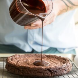Chocolate glaze being poured onto a flourless chocolate cake.