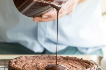 Chocolate glaze being poured onto a flourless chocolate cake.