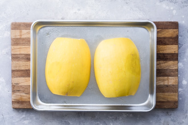 Two halves of a yellow squash on a baking sheet.