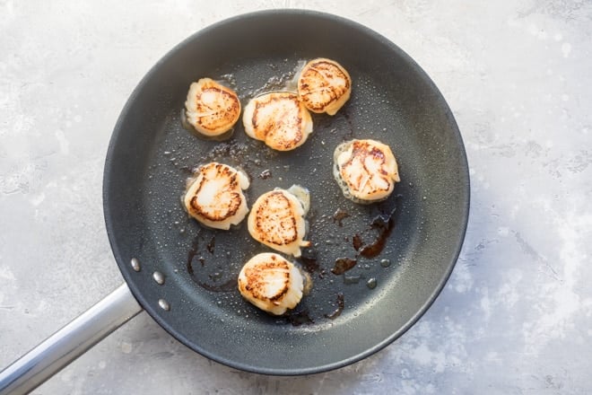 Pan-seared scallops in a black pan.