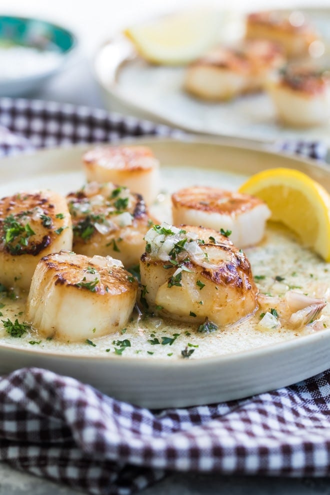 Pan-seared scallops with a lemon butter sauce on a white plate.