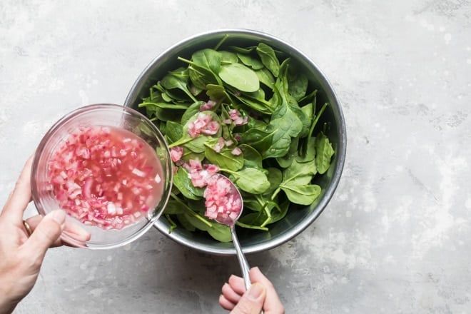 Hot bacon dressing being poured on to a bowl of spinach.