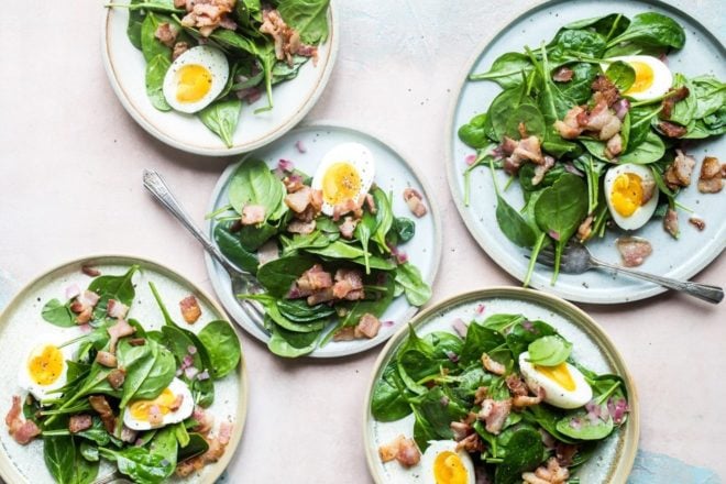 Spinach salad with bacon dressing on white plates.