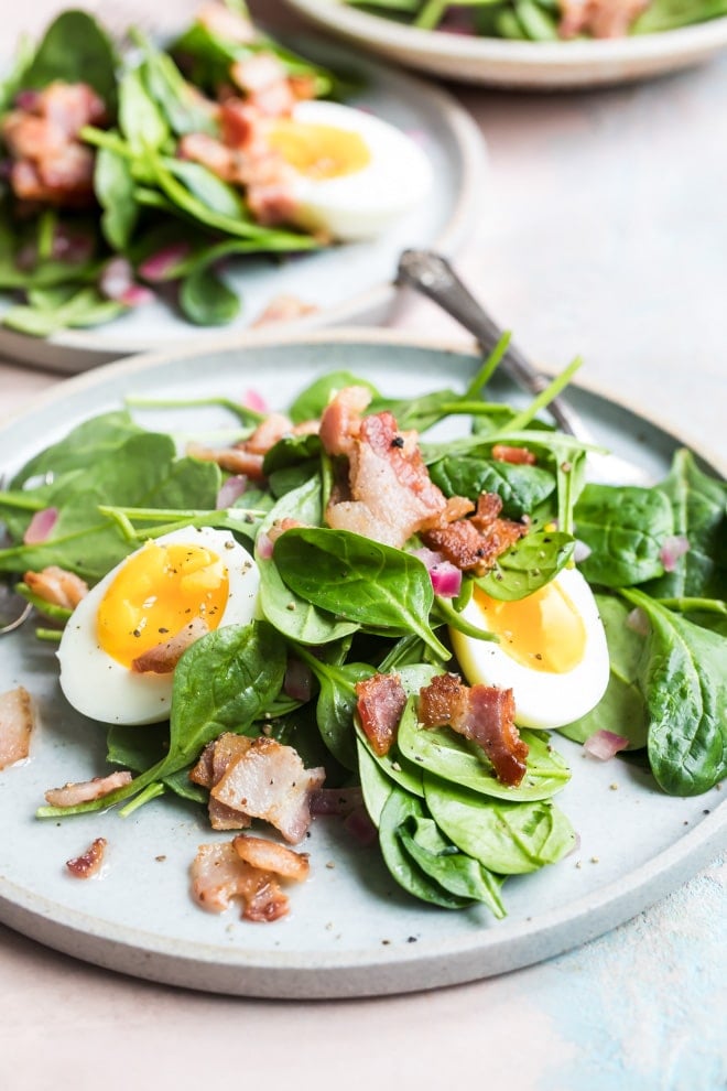Spinach salad with bacon dressing on a white plate.