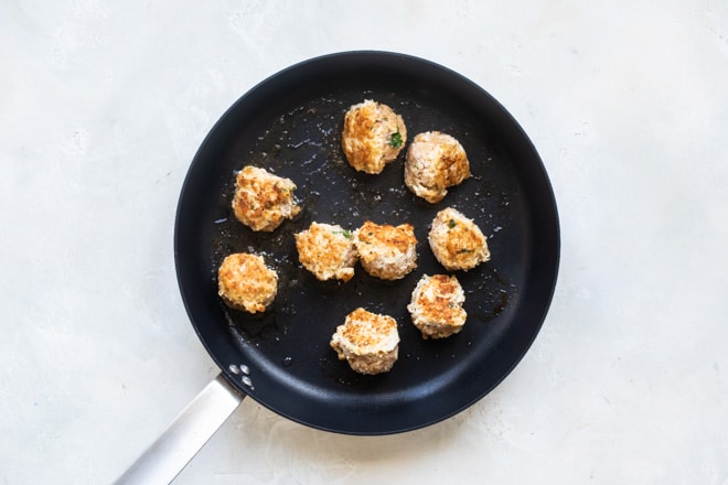 Chicken meatballs cooking on a black skillet.