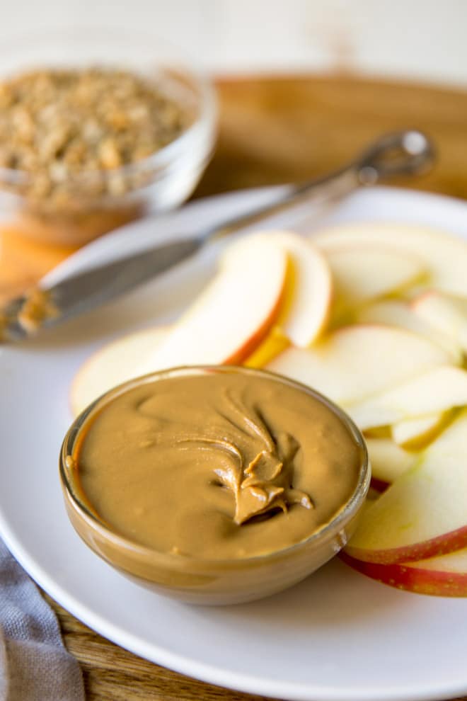 Homemade sunflower seed butter in a dish on a white plate with apple slices.