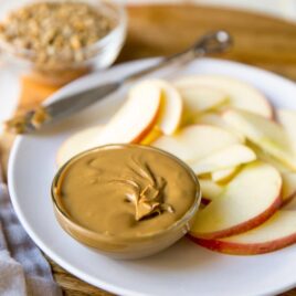 Homemade sunflower seed butter in a dish on a white plate with apple slices.