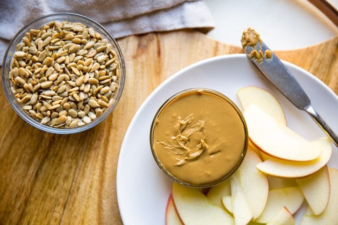 Homemade sunflower seed butter in a dish on a white plate with apple slices.